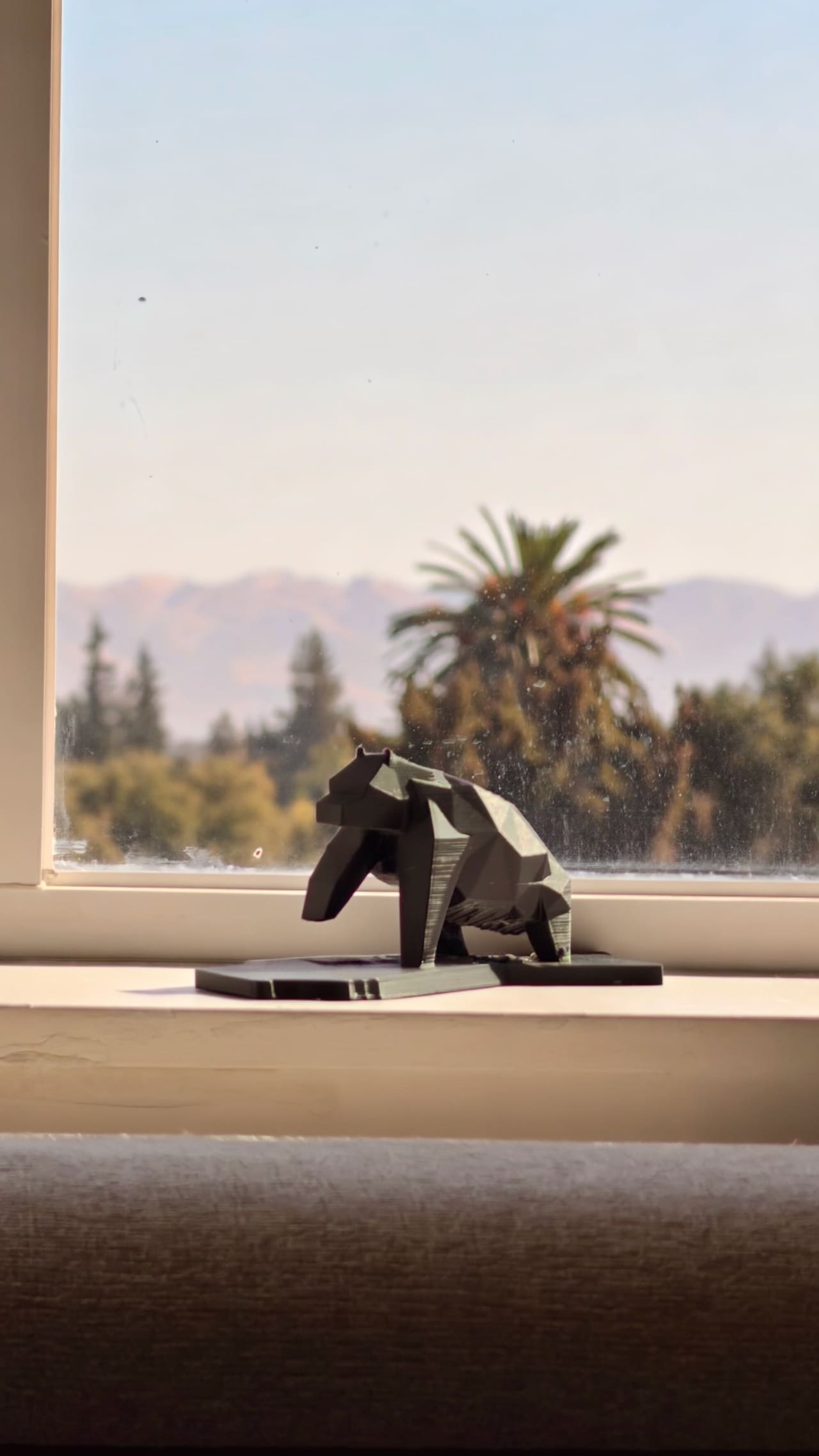 A low-poly bear printed in black PLA, standing on a base shaped like California, a palm tree outside the window